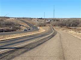 A road in Texas set against a blue sky with two white pick-up trucks approaching in the distance.