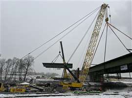 The floating crane holds the weight of the larhe bridge section while the onshore crane hoists a smaller section away.