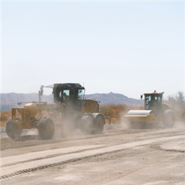 Working in extreme conditions, a Cat CS13 GC soil compactor follows a grader on a road constrction project