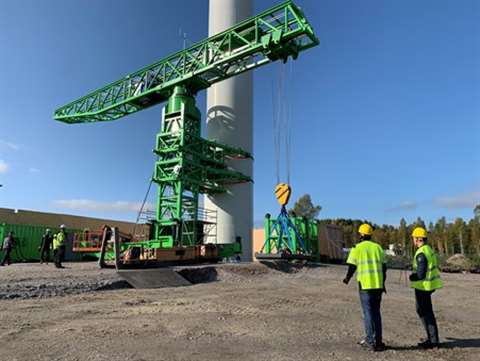 Green small lattice tower type crane at the base of a wind turbine tower