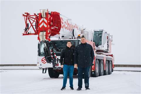 White and red wheeled crane, boom down, with two people standing in front of it
