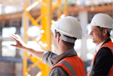 Two construction workers on a construction site, with one pointing at something in the distance.