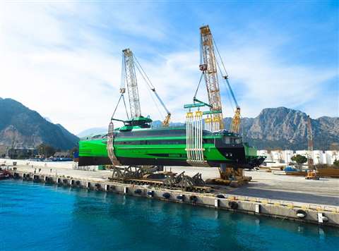 pair of big Demag crawler cranes lifting a bright green boat