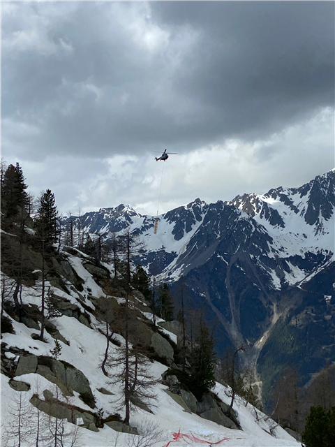 A helicopter transports a crane section over the French Alps