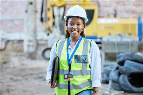 A women in a high-vis vest hard hard hat smiles while standing on a construction site