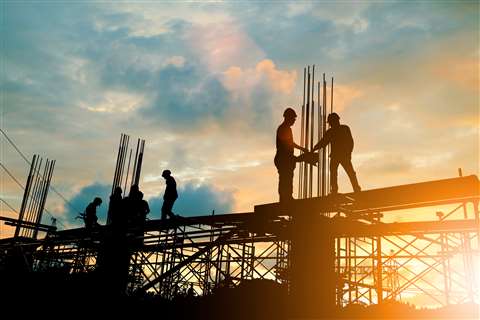 Construction workers and scaffolding in silhouette against a sunset