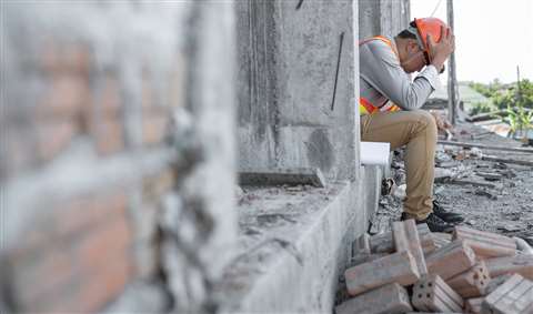 A construction worker sits on a step and holds his head in his hands on a messy construction site