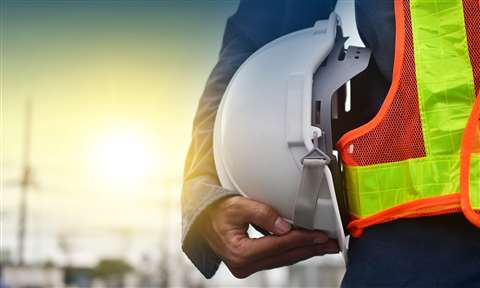 Close-up of a white hard hat held against a construction worker's hip to illustrate news of the safest construction companies