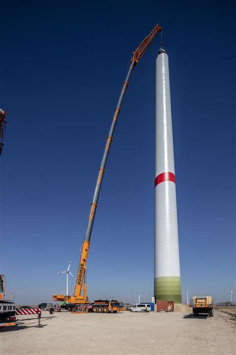 Sommer Kranverleih's new bright yellow Liebherr LTM 1450-8.1 on its first job lifting at a hook height of 100 metres. Red and white wind turbine tower against a blue sky