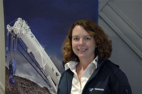 Julie Fuller, red hair, blue clothes, standing in front of a picture of a white crane boom