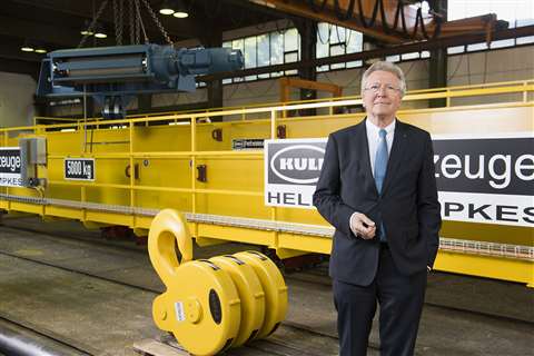 Heinz Helmut Kempkes, smart, in factory in front of a big yellow EOT crane bridge and hookblock