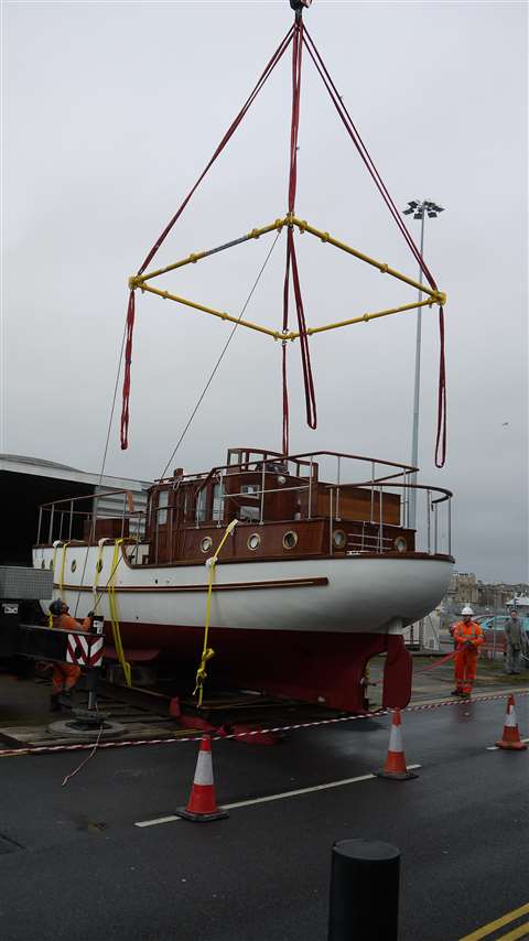 Small white vessel named Dorian ready to be lifted wit hte four point yellow spreader frame suspended form green King Lifting Liebherr AT crane